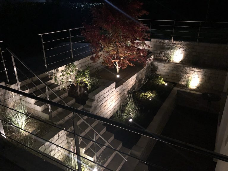 Blick von oben in einen beleuchteten Lichthof mit Treppe und Pflanzbeeten.