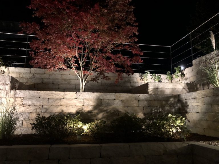 Abends beleuchteter Lichthof mit Natursteinmauer, Pflanzen und rotem Fächerahorn.