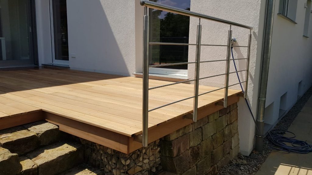 Erhöhte Holzterrasse mit Metallgeländer und kleinem Treppenabgang.