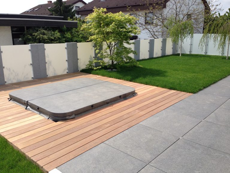 Holzdeck mit abgedecktem Whirlpool neben Rasen und heller Terrasse.