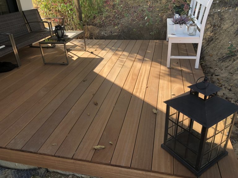 Holzterrasse mit Gartenstühlen, Pflanzkasten und Laterne.