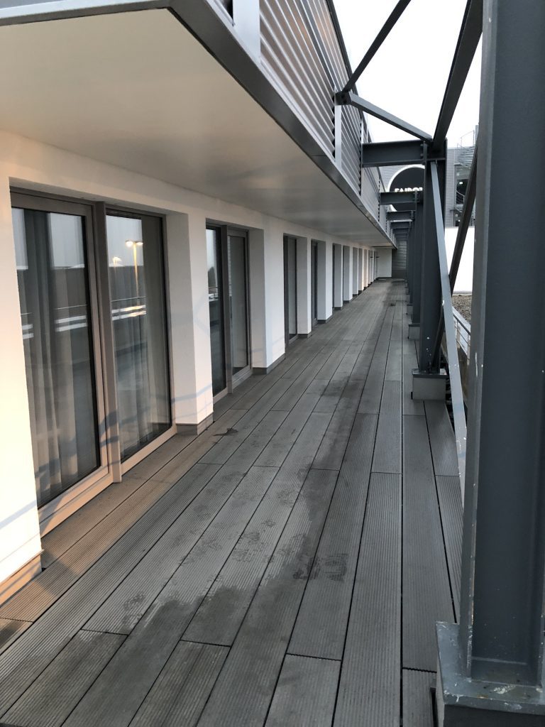 Schmale Holzterrasse entlang der Fensterfront eines Gebäudes.