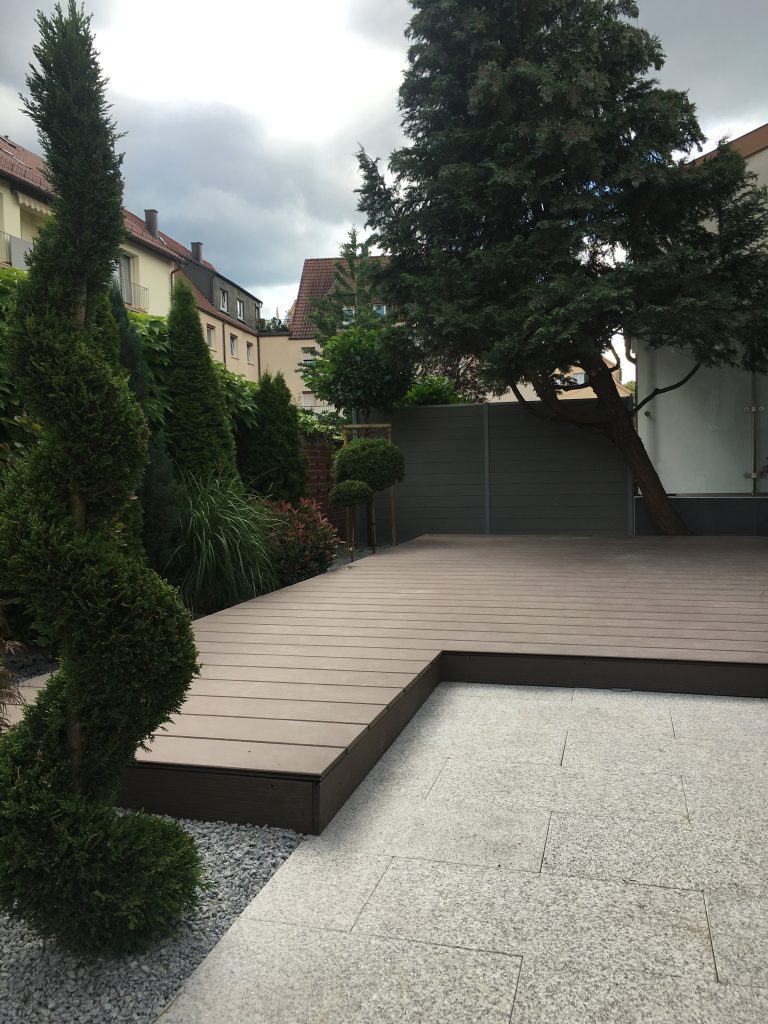 Abgestufte helle Terrasse zwischen Sträuchern und geschnittenen Gehölzen.