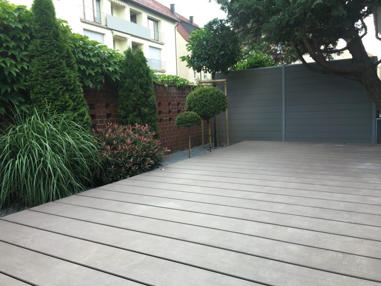 Helle Terrasse mit breiten Dielen und bepflanzter Garteneinfassung.