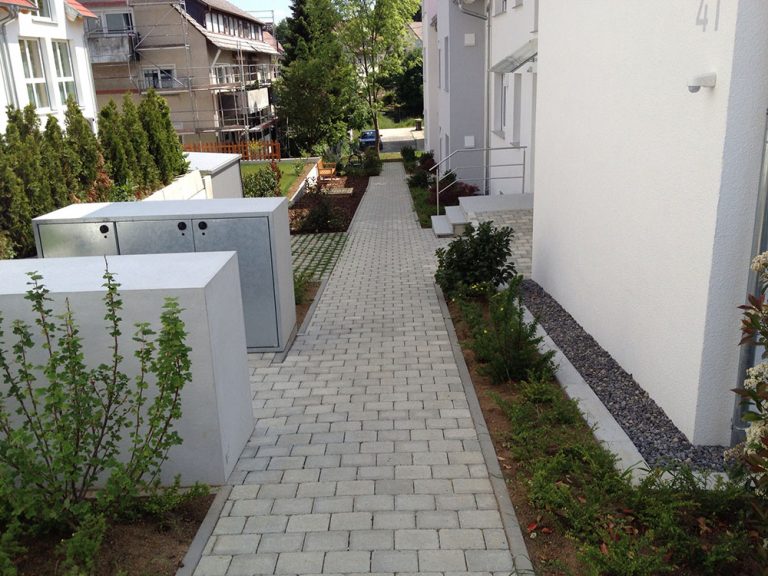 Schmaler gepflasterter Zugangsweg mit seitlichen Pflanzbeeten am Wohnhaus.