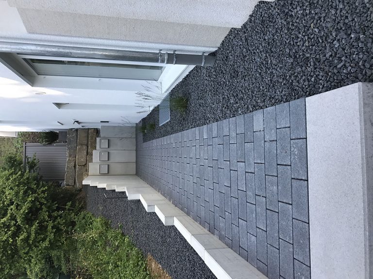 Gepflasterter Seitenweg mit grauem Kiesstreifen am Gebäude.