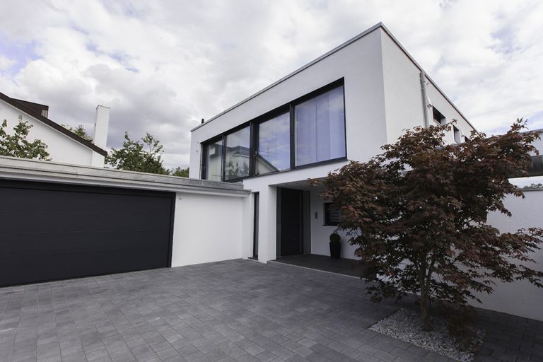 Breite gepflasterte Einfahrt vor einer Doppelgarage und einem modernen Wohnhaus.