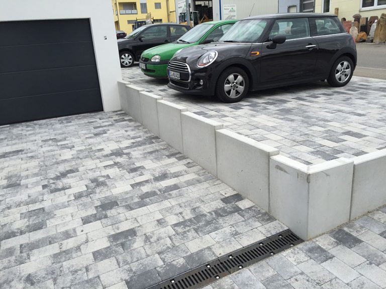 Mit Mauerscheiben eingefasster Stellplatz über einer gepflasterten Zufahrt.