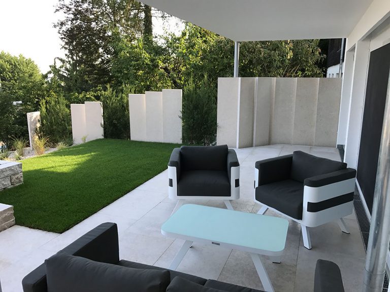 Sitzgruppe auf einer Terrasse mit Rasen und hellem Sichtschutz.