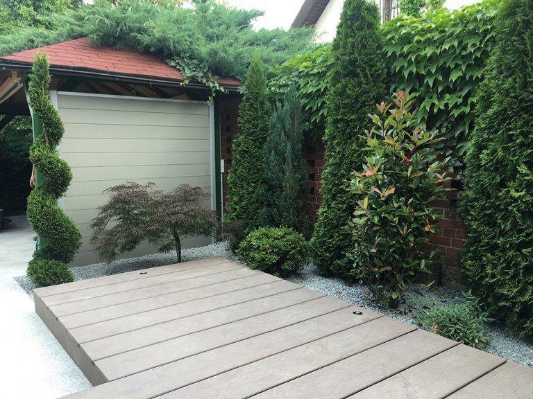 Heller Terrassenbelag mit begrüntem Sichtschutz und geschnittenem Ziergehölz.