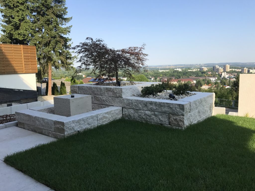 Terrassierter Garten mit hellen Natursteinmauern und Rasenfläche.