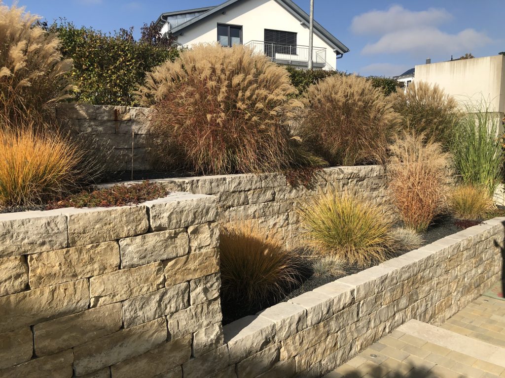 Gestaffelte Natursteinmauern mit Ziergräsern in herbstlicher Färbung.
