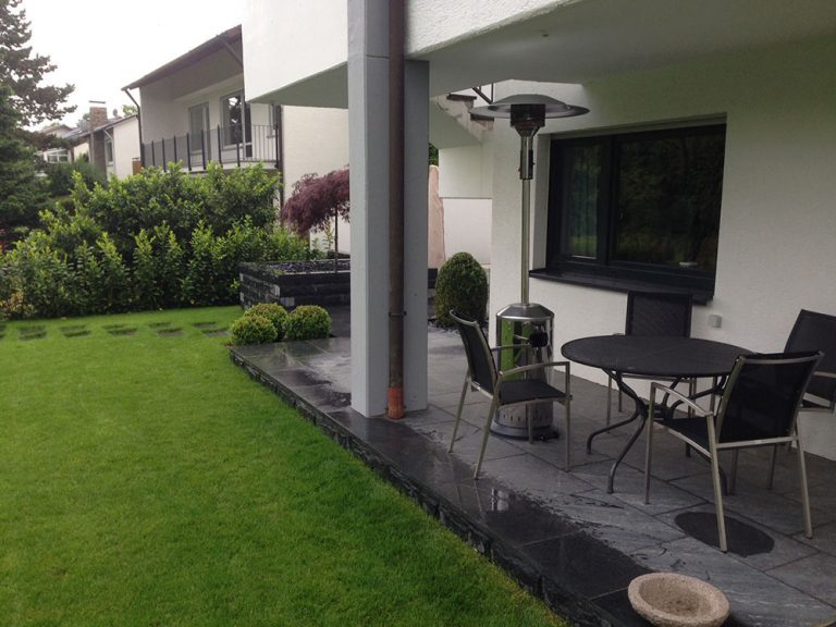 Überdachter Sitzplatz am Haus mit angrenzendem Gartenrasen.