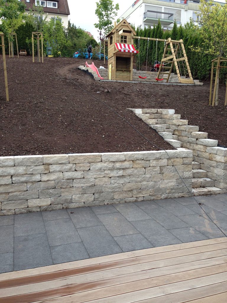 Frisch angelegtes Gartenbeet hinter einer Natursteinmauer und Terrasse.