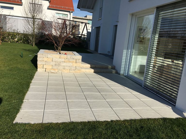 Terrasse aus grauen Platten mit Naturstein-Stützmauer am Wohnhaus.