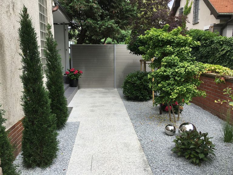 Gartenweg aus hellen Platten mit Kiesbeeten, schlanken Gehölzen und Formschnitt.