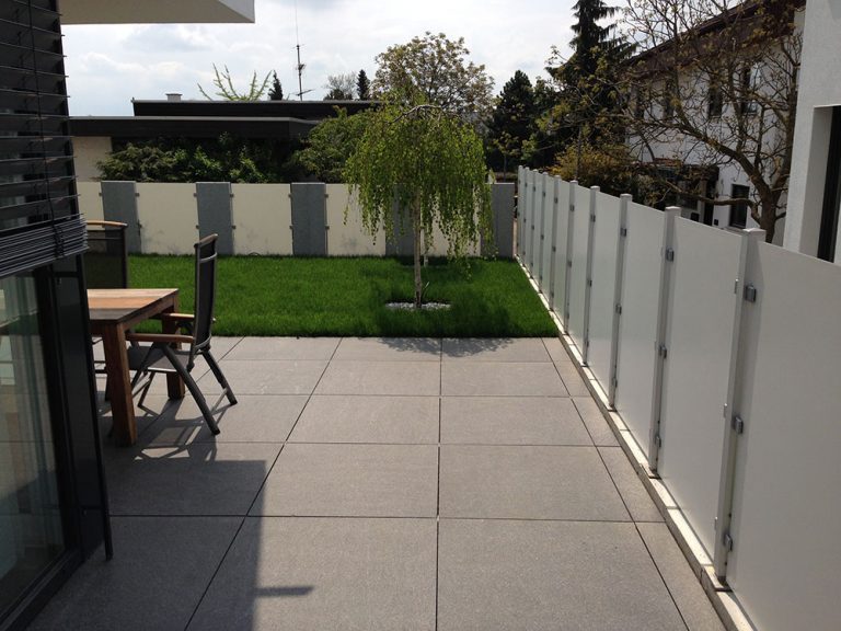Großformatige Terrassenplatten mit hellem Sichtschutz neben einer Rasenfläche.