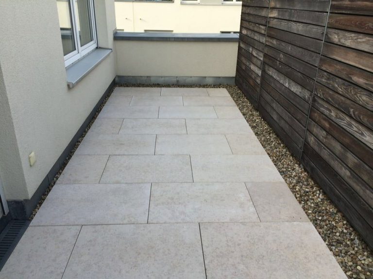 Schmaler Terrassenbereich mit hellen Platten und dunkler Holzwand.