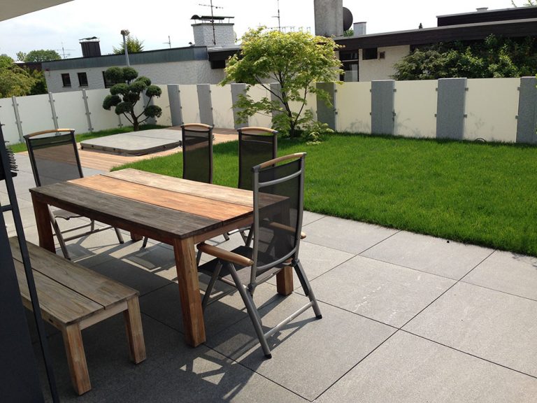 Terrasse mit Esstisch und Stühlen vor einer grünen Rasenfläche.