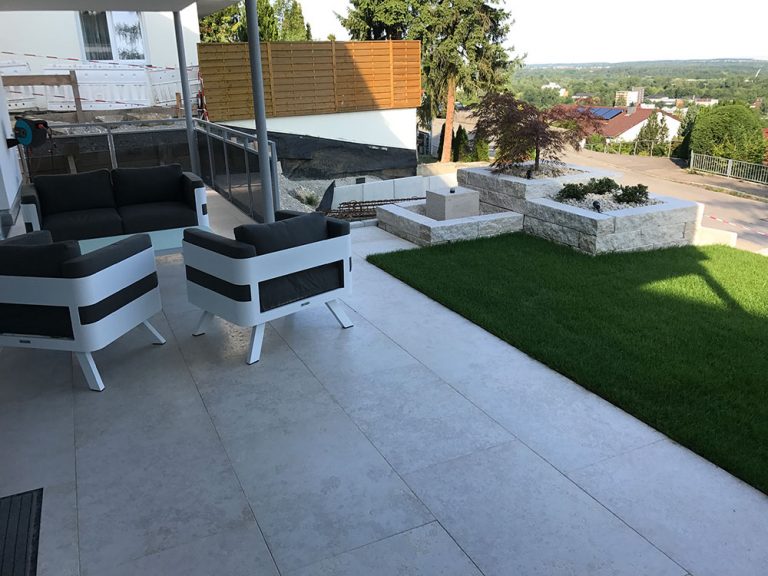Gartenlounge auf einer hellen Terrasse mit Rasen und Natursteineinfassungen.
