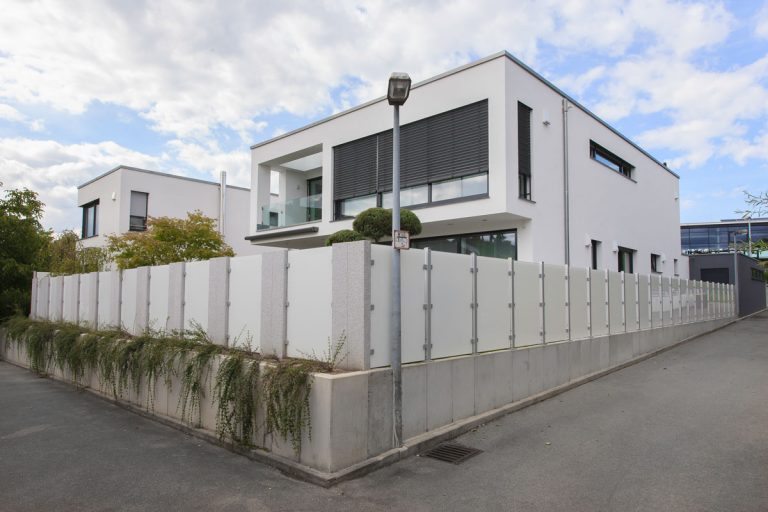 Eckgrundstück mit modernem Wohnhaus und Sichtschutz aus hellen Elementen.