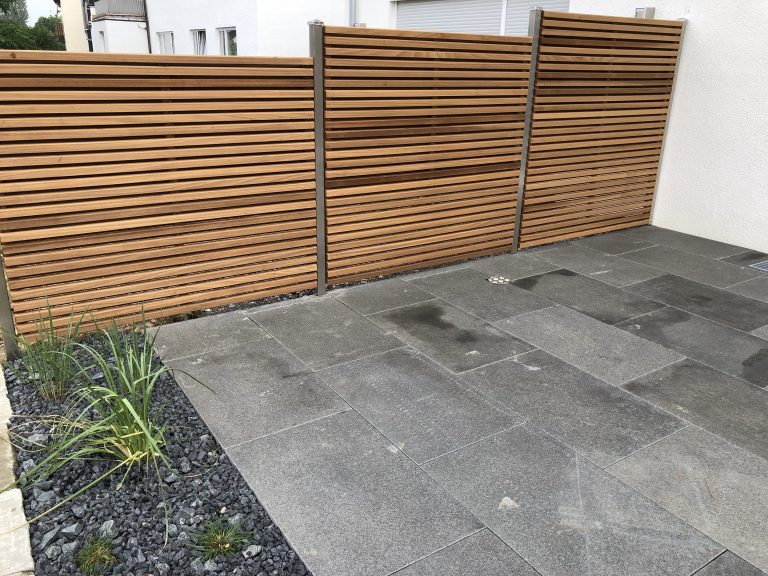 Holzlamellen-Sichtschutz hinter einer Terrasse aus grauen Platten.