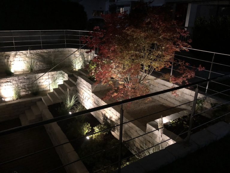 Roter Ahorn und warm beleuchtete Natursteinmauern in einem abgesenkten Gartenbereich.