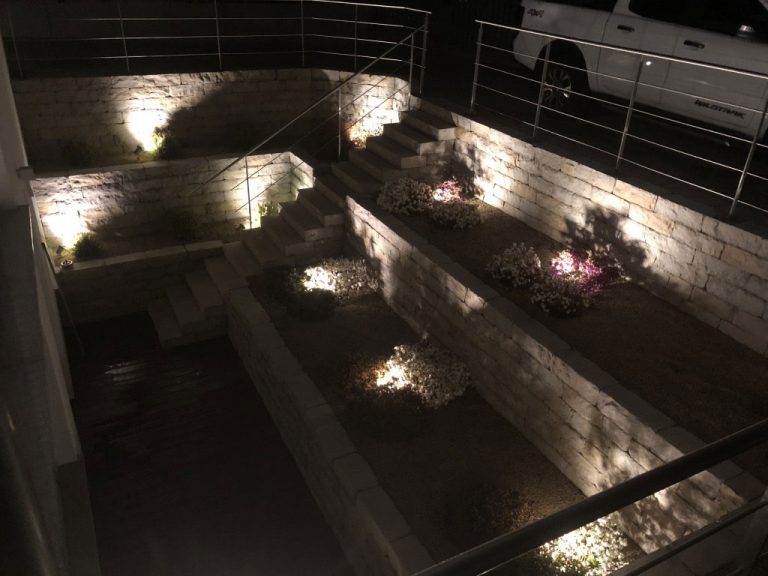 Beleuchtete Natursteinmauern und Treppenstufen in einem Lichthof.