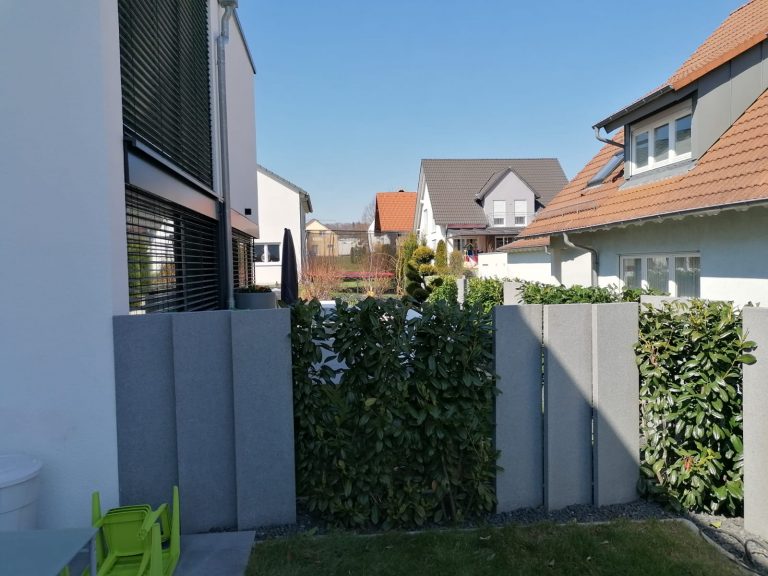 Helle Sichtschutzstelen mit dichtem Grün zwischen benachbarten Häusern.