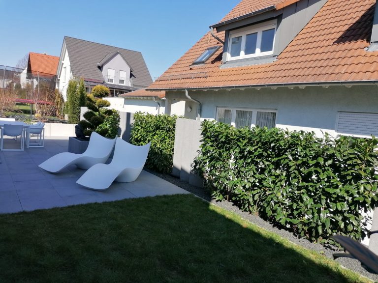 Gartenlounge mit weißen Liegen, Rasen und begrüntem Sichtschutz.