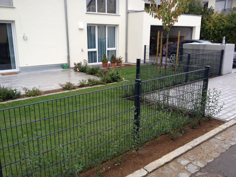 Metall-Gartenzaun mit Tor vor einem Rasenstreifen am Wohnhaus.