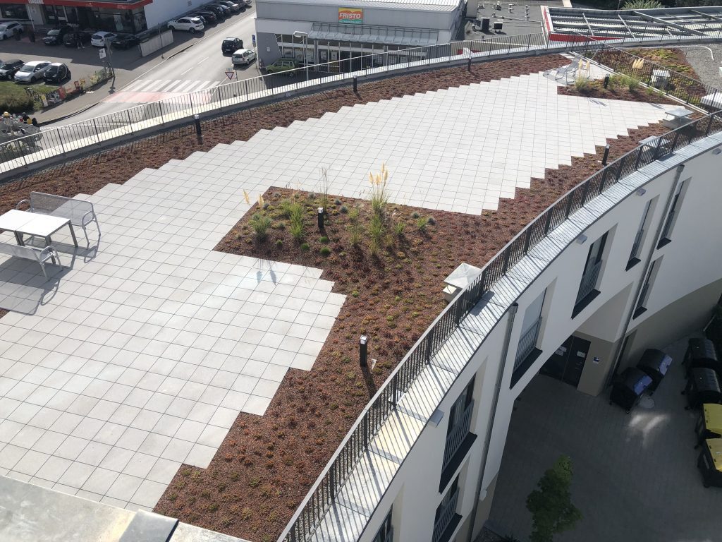 Dachterrasse mit hellen Platten und umlaufenden Pflanzbeeten aus der Vogelperspektive.