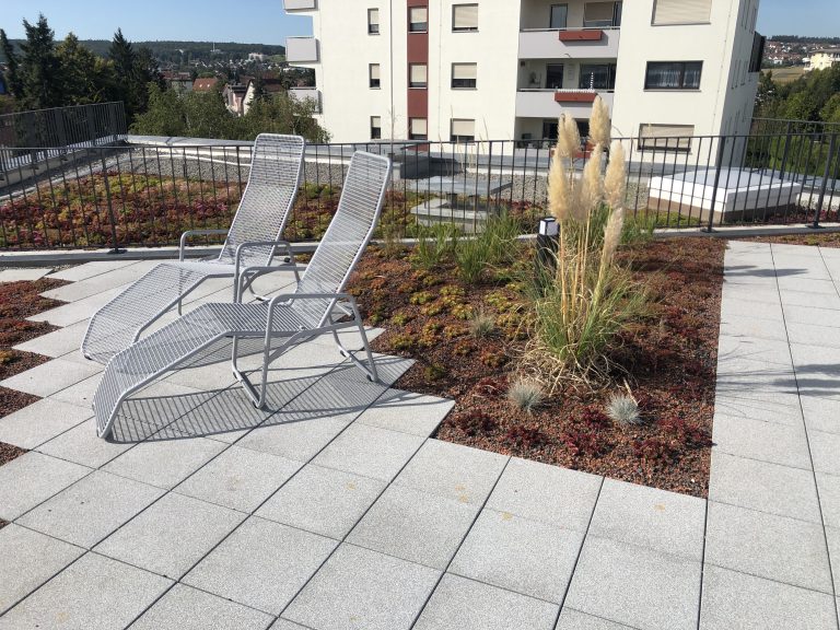 Liegestühle auf einer Dachterrasse neben Gräsern und Stauden.