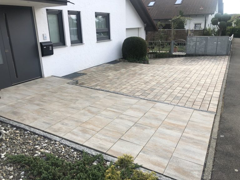 Gepflasterter Eingangsbereich mit großen hellen Platten vor einer Haustür.
