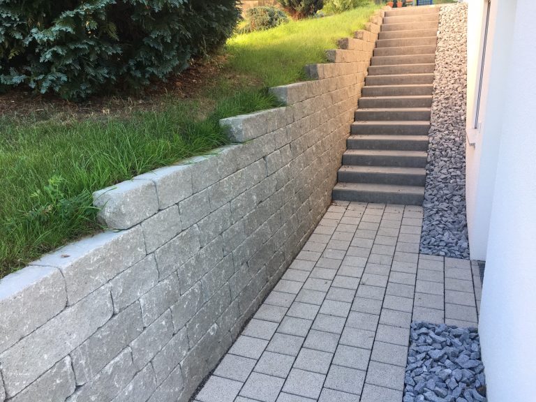 Naturstein-Stützmauer mit Rasenböschung neben einem Treppenweg.