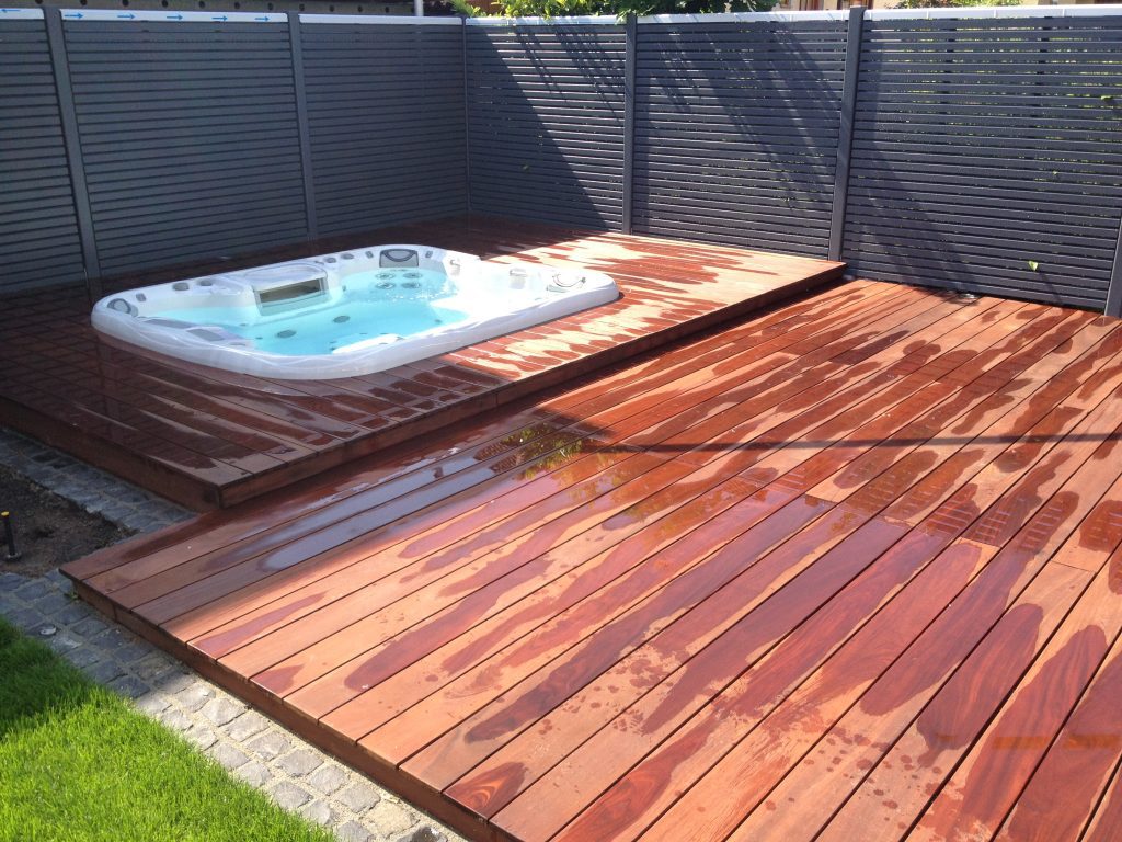 Whirlpool mit gestuften Holzdielen und dunklem Sichtschutz im Garten.