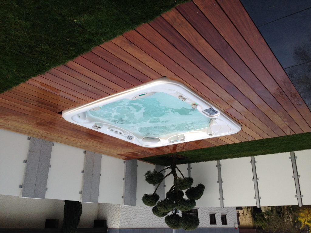 Whirlpool in einer Holzterrasse mit angrenzender Rasenfläche und Sichtschutz.