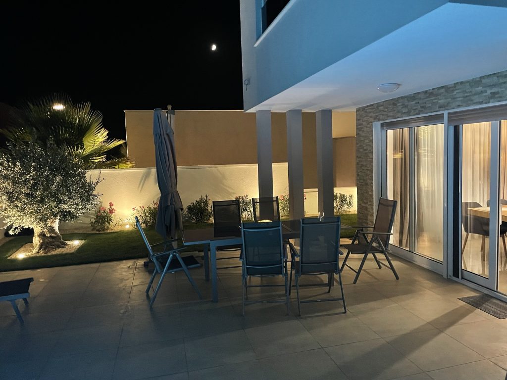 Abendlich beleuchtete Terrasse mit Essgruppe vor einer Glasfront.