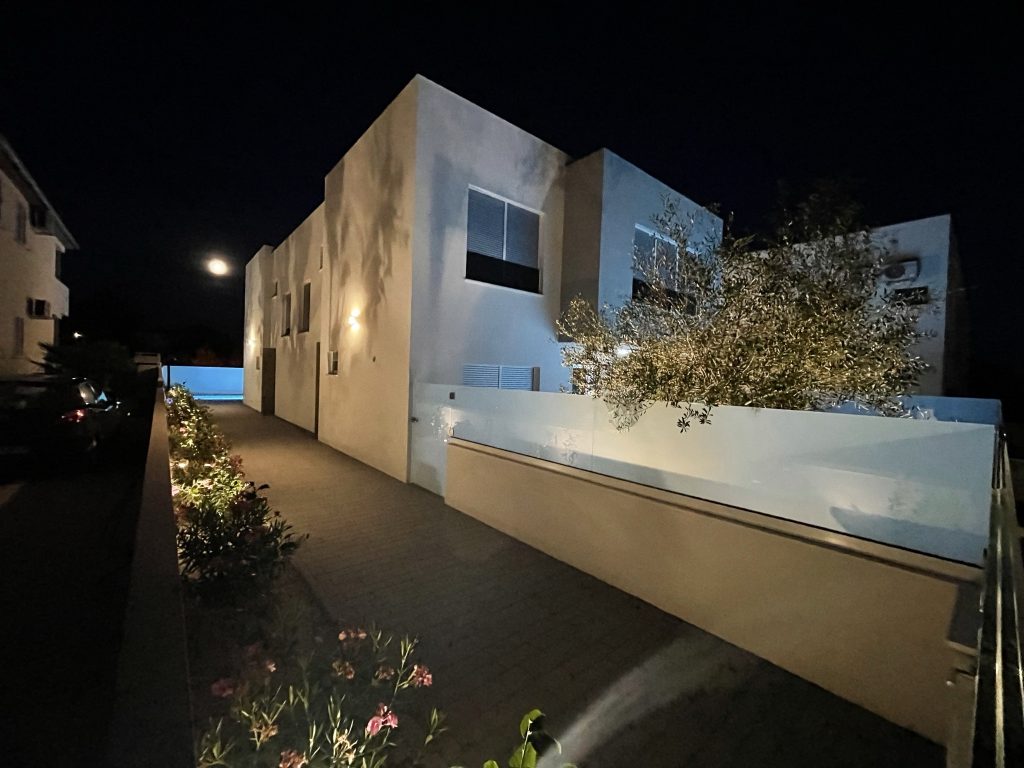 Abendansicht einer beleuchteten Einfahrt neben einem modernen Wohnhaus.