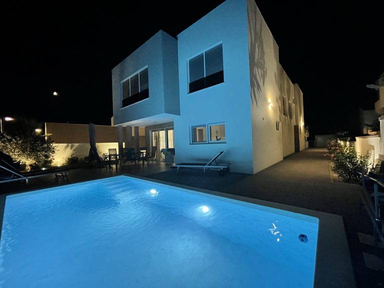 Beleuchteter Gartenpool vor einem modernen Wohnhaus bei Nacht.