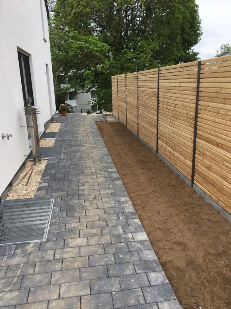 Schmaler Hausweg neben einem langen Sichtschutz aus Holzlamellen.