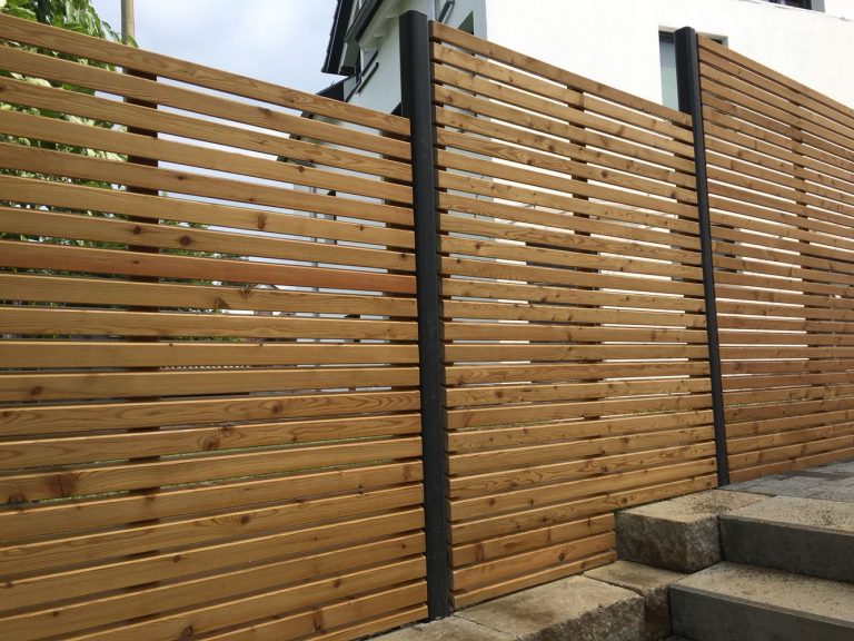 Sichtschutzwand aus waagerechten Holzlamellen neben einer Pflasterfläche.