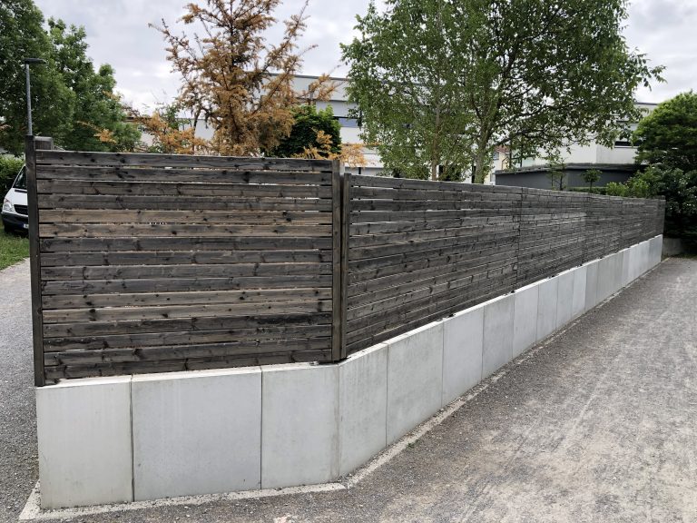 Dunkler Holz-Sichtschutz auf einer hellen Stützmauer entlang des Grundstücks.