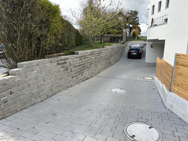 Gepflasterte Zufahrt neben einer langen Natursteinmauer.