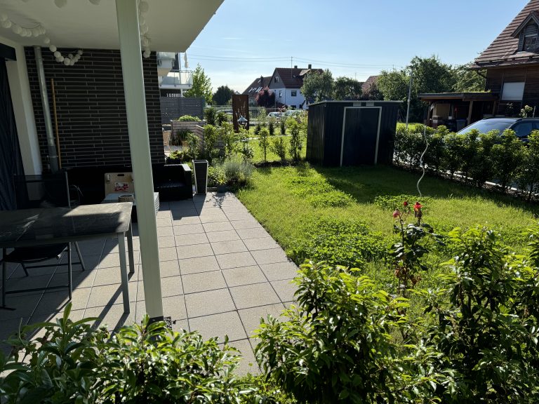 Gartenterrasse mit Plattenbelag und locker bepflanztem Grünbereich.