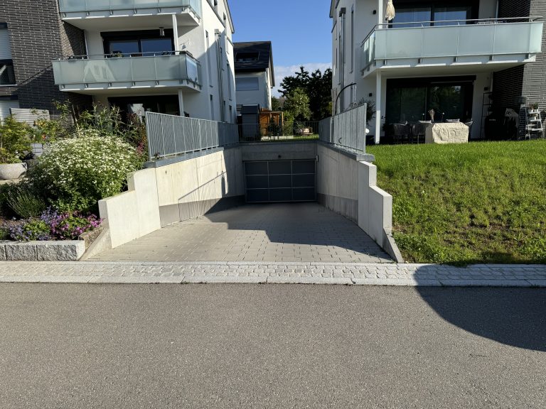 Treppenzugang zwischen hellen Stützwänden und bepflanzten Böschungen.