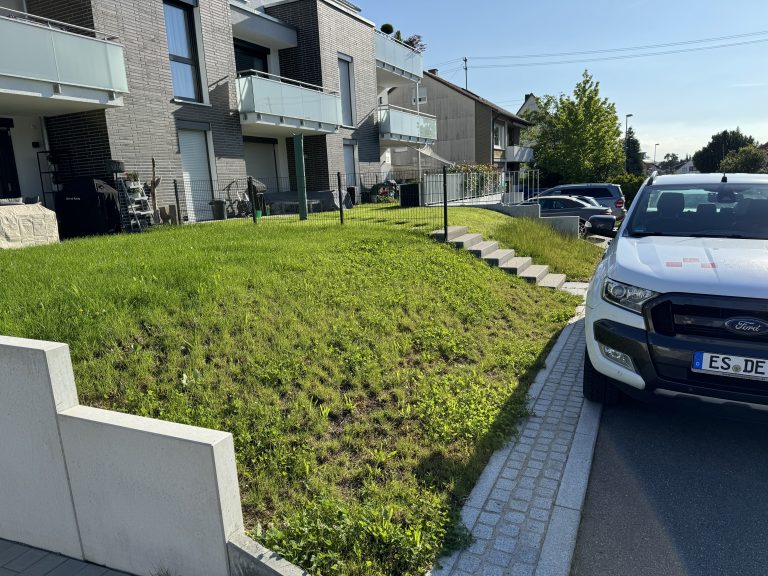 Bepflanzte Böschung mit hellen Stützwänden an einer Wohnstraße.