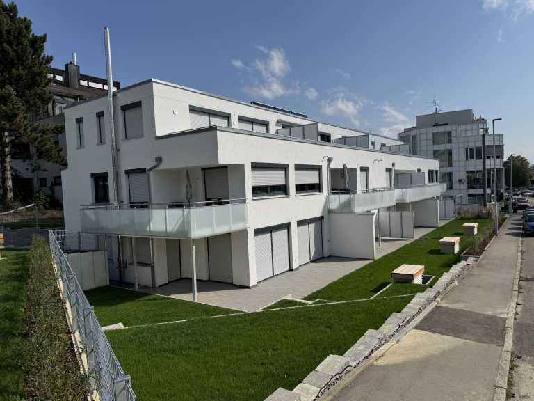 Terrassierte Außenanlage mit Rasen vor modernen Wohnhäusern.