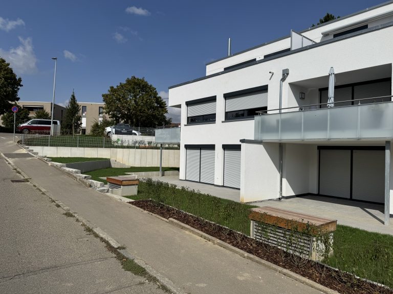 Wohnhaus mit Garagen, gepflasterten Zufahrten und Rasenflächen entlang der Straße.